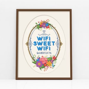 以下が含まれることがあります： 「WIFI SWEET WIFI」の文字が青色で刺繍された、花柄のリースで囲まれた額入りのクロスステッチアート。作品は楕円形で、コードQWERT2671が含まれています。フレームは茶色です。