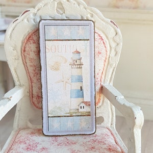 May include: A vintage-style sign with a lighthouse and the word "SOUTH" on a blue and white background. The sign is framed in a light brown wood frame.