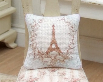 May include: A white chair with a floral patterned cushion and a pillow with a brown Eiffel Tower design. The pillow has a wreath of leaves around the tower.