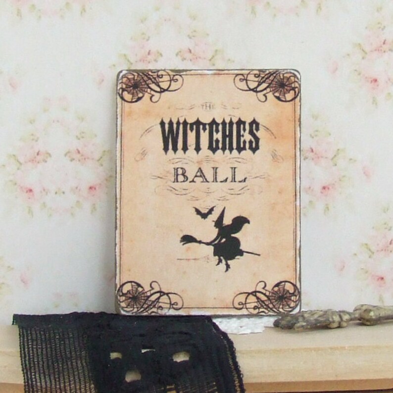 K&ouml;nnte beinhalten: Rechteckiges Schild mit dem Text "THE WITCHES BALL" in einer Vintage-Schrift, mit einer Silhouette einer Hexe auf einem Besen und Flederm&auml;usen. Das Schild hat dekorative Eckelemente und ein verwittertes Aussehen, perfekt f&uuml;r Halloween.