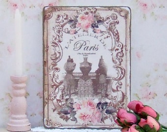 Puede incluir: Un letrero de estilo vintage con un diseño floral y el texto "L'Atelier de Paris" en una fuente decorativa. El letrero está enmarcado en un marco de madera marrón y tiene un aspecto desgastado.