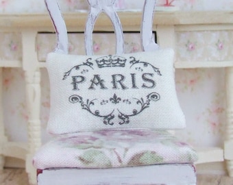 May include: A white chair with a floral patterned cushion and a white pillow with a black crown and the word "PARIS" printed on it.
