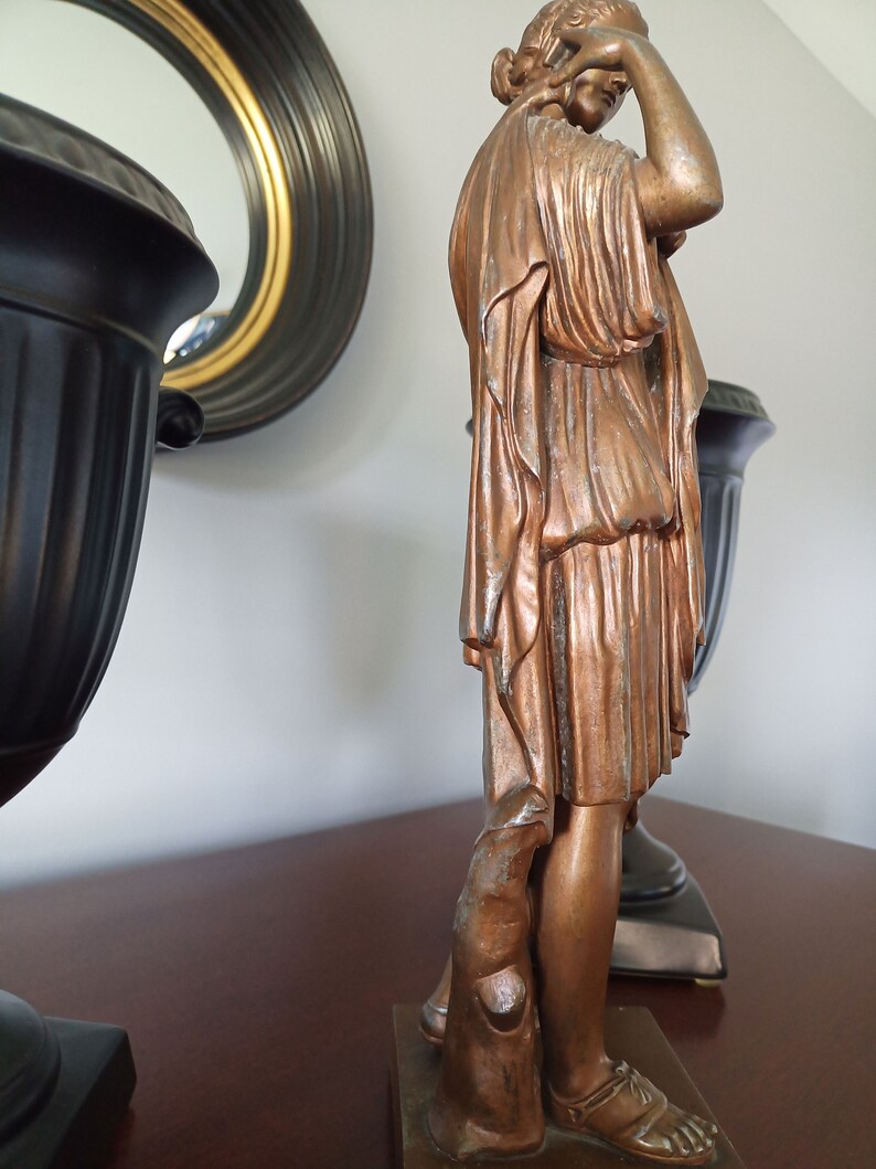 May include: A bronze statue of a woman in a flowing robe, standing on a base with a smaller bronze statue of a dog at her feet.