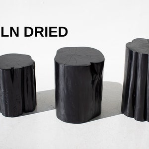 May include: Three black wooden stools, made from kiln dried wood, are arranged in a row from smallest to largest. The stools are all round and have a natural wood grain.