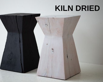 May include: Two wooden stools, one black and one white, with a unique hourglass shape. The stools are made from kiln dried wood and have a natural, rustic look. KILN DRIED text is visible in the image.