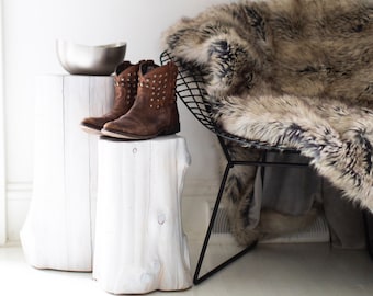Può includere: Due stivali da cowboy in pelle marrone con borchie metalliche su uno sgabello di legno bianco. Un copridivano in pelliccia sintetica è drappeggiato su una sedia in filo metallico nero.