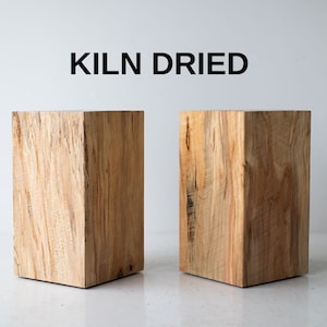 May include: Two wooden blocks, each with a different wood grain pattern, are shown on a white surface. The blocks are rectangular and have a natural wood finish. The text "KILN DRIED" is displayed above the blocks.