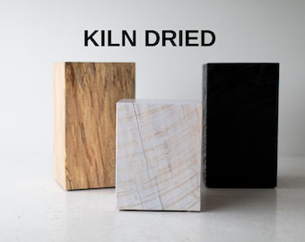 May include: Three wooden blocks, one light brown, one white, and one black, with the text "KILN DRIED" above them.