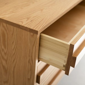 May include: A wooden dresser with drawers that open to reveal a light wood interior. The drawers have a simple design and are made of solid wood.