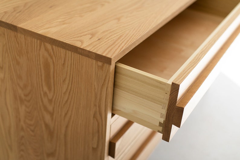 May include: A wooden dresser with drawers that open to reveal a light wood interior. The drawers have a simple design and are made of solid wood.