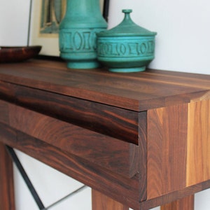 May include: A dark wood console table with two drawers and a black metal X-shaped base. The table is decorated with two teal ceramic vases.