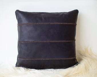 Puede incluir: Una almohada de cuero azul oscuro con costuras decorativas. La almohada es de forma cuadrada y tiene una superficie suave y texturizada.