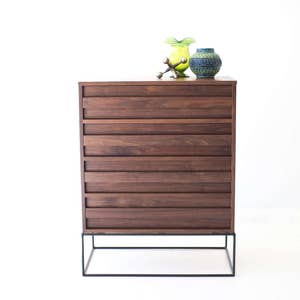 Pu&ograve; includere: Com&ograve; in legno marrone scuro in stile moderno della met&agrave; del secolo, con sei cassetti. Ha una base in metallo nero. Due vasi decorativi e una scultura in metallo sono sopra. Il com&ograve; &egrave; alto circa 76 cm.