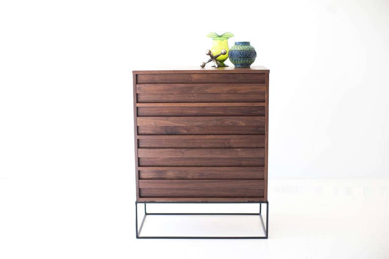 Pu&ograve; includere: Com&ograve; in legno marrone scuro in stile moderno della met&agrave; del secolo, con sei cassetti. Ha una base in metallo nero. Due vasi decorativi e una scultura in metallo sono sopra. Il com&ograve; &egrave; alto circa 76 cm.