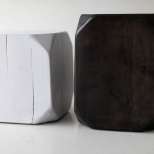 May include: Two wooden cube stools, one painted white and the other stained dark brown. The stools have a geometric shape with rounded edges.