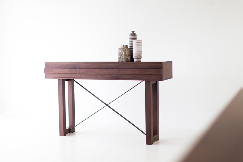 May include: A dark brown wooden console table with a black metal X-shaped base. The table has three drawers and is decorated with three ceramic vases.