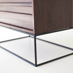 Pu&ograve; includere: Un mobile moderno in legno scuro con tre cassetti. Il mobile &egrave; sostenuto da una struttura in metallo nero geometrica. Il design &egrave; minimalista e la venatura del legno &egrave; visibile.