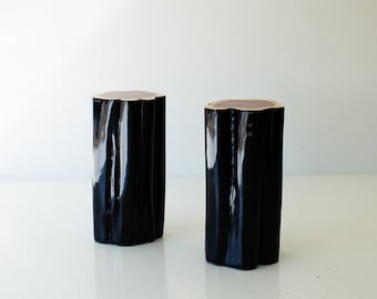 May include: Two black, wooden, cylindrical stools with a wavy, organic design. The stools are made of wood and have a glossy black finish.