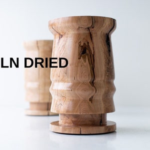 May include: Two wooden stools with a unique, organic shape. The stools are made from kiln-dried wood and have a natural finish. The text "KILN DRIED" is visible in the image.