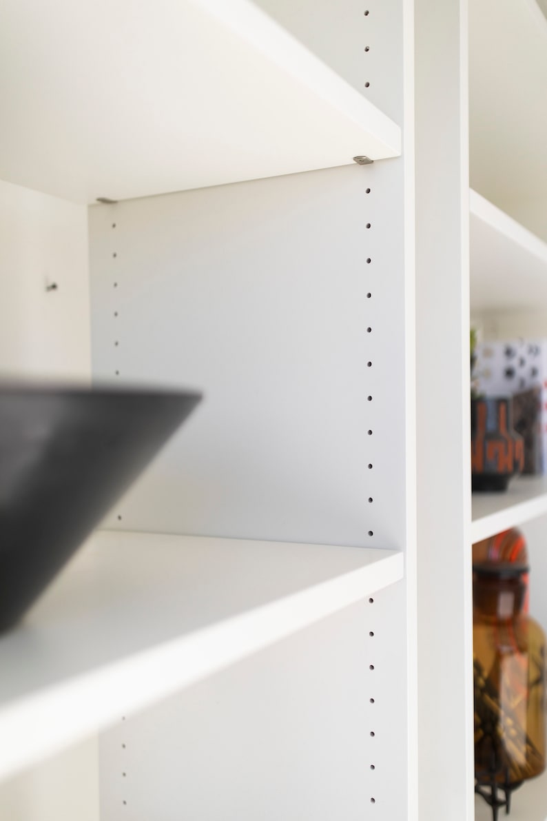 May include: White bookshelf with adjustable shelves. The shelves are made of white wood and have a smooth finish. The shelves are adjustable and can be moved to different heights.