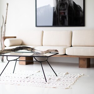 Pode incluir: Um sof&aacute; branco com uma fotografia de um cavalo emoldurada em preto acima. Uma mesa de centro de vidro com uma base de madeira fica na frente do sof&aacute;. Um ramo de madeira flutuante &eacute; colocado em cima da mesa. Um tapete branco com um padr&atilde;o preto est&aacute; no ch&atilde;o.