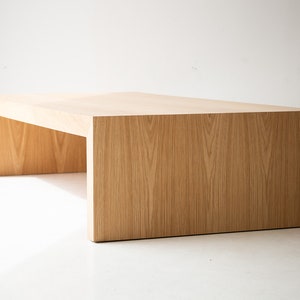 May include: A light wood coffee table with a rectangular top and a unique open frame design. The table is made of solid wood and has a natural finish.