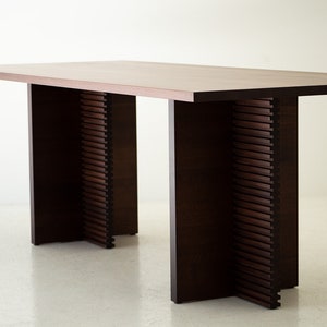 May include: A dark brown wooden table with a rectangular top and two sets of legs. Each leg is made of stacked wooden slats that create a unique design.