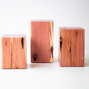 May include: Three rectangular wooden blocks of varying heights. The blocks are made of reddish-brown wood with visible grain and natural knots. The blocks are arranged on a white surface.