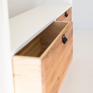 May include: A white cabinet with two wooden drawers. The drawers have black leather pulls. The top drawer is closed and the bottom drawer is open.