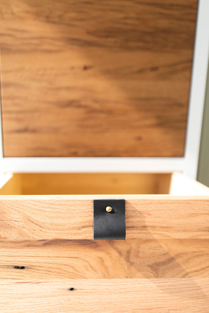 May include: A wooden drawer with a black leather pull and a gold metal knob. The drawer is open and the wood grain is visible.