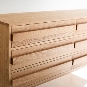May include: A light wood dresser with six drawers and a simple design. The dresser has a natural wood finish and is supported by four slender legs.