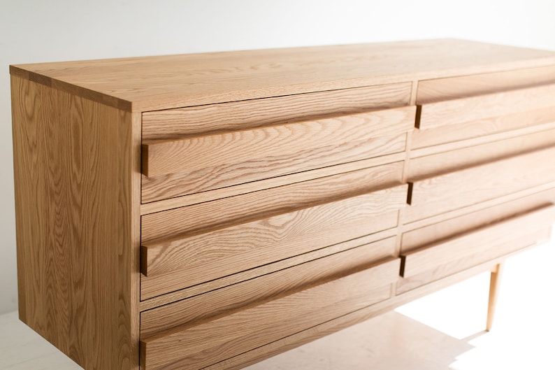 May include: A light wood dresser with six drawers and a simple design. The dresser has a natural wood finish and is supported by four slender legs.