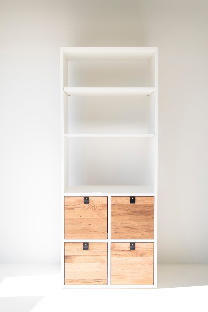 May include: White bookshelf with four wooden drawers. The drawers have black metal handles and are made of reclaimed wood.