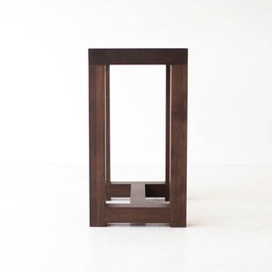 Puede incluir: Una mesa de madera marr&oacute;n oscuro con un dise&ntilde;o simple y rectangular. La mesa tiene una tapa cuadrada y cuatro patas, cada una con una secci&oacute;n cuadrada. La mesa est&aacute; hecha de madera maciza y tiene un acabado natural.
