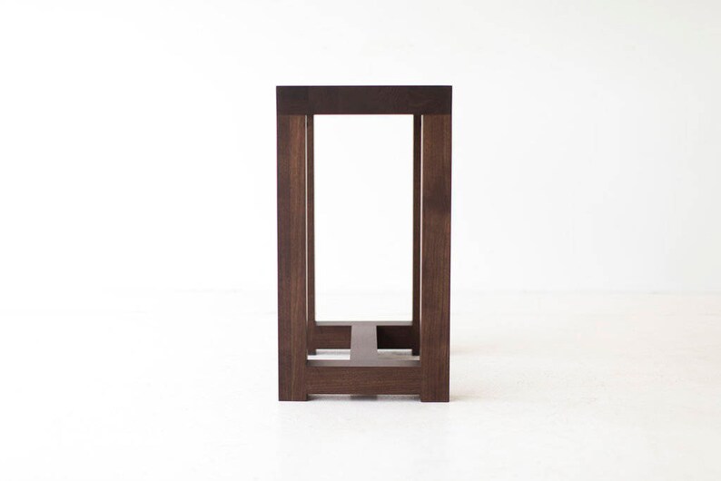 Puede incluir: Una mesa de madera marr&oacute;n oscuro con un dise&ntilde;o simple y rectangular. La mesa tiene una tapa cuadrada y cuatro patas, cada una con una secci&oacute;n cuadrada. La mesa est&aacute; hecha de madera maciza y tiene un acabado natural.