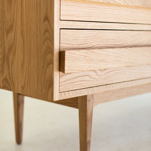 May include: A wooden dresser with four drawers and tapered legs. The drawers have a simple, minimalist design with no visible handles.
