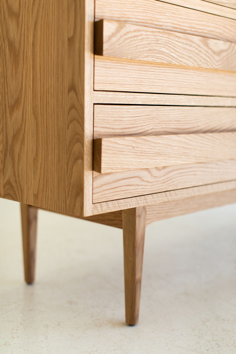 May include: A wooden dresser with four drawers and tapered legs. The drawers have a simple, minimalist design with no visible handles.