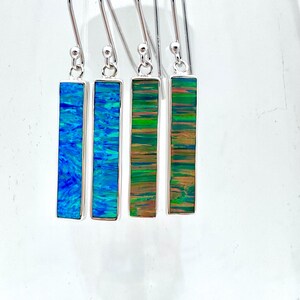 May include: Four pairs of silver dangle earrings with rectangular opal stones. The stones are blue, green, and brown with iridescent shimmer.