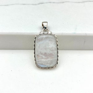 May include: A rectangular pendant with a polished, iridescent moonstone. The stone is set in a silver-colored metal frame with a decorative rope-like border. The pendant has a small loop at the top for a chain.