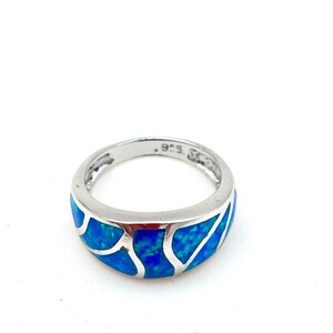 May include: A silver ring with a blue opal inlay. The opal has a swirling pattern and is set in a silver band.