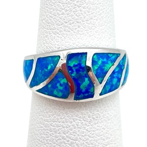 May include: A silver ring with a blue and green opal inlay. The opal is set in a geometric pattern.