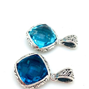 May include: Two silver pendants with blue gemstone accents. Each pendant features a square-shaped gemstone with intricate silver detailing around the edges.
