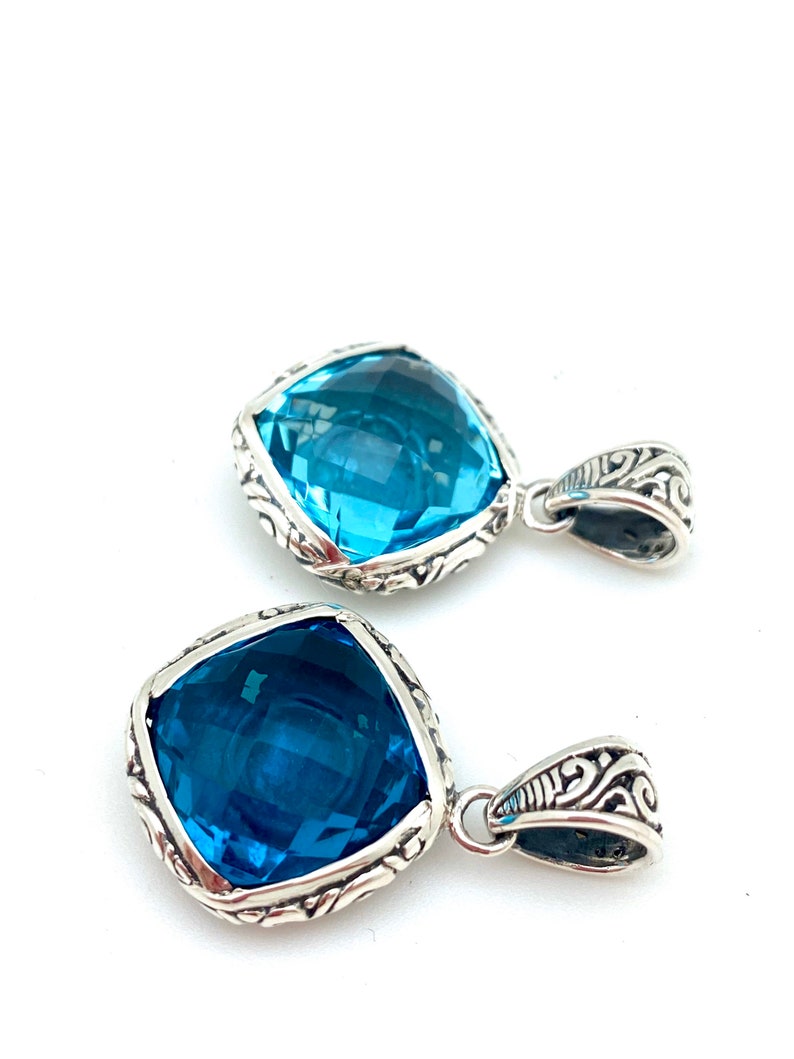 May include: Two silver pendants with blue gemstone accents. Each pendant features a square-shaped gemstone with intricate silver detailing around the edges.
