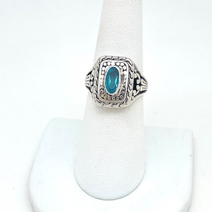 May include: A silver ring with a blue gemstone set in a square bezel. The ring has a textured band.