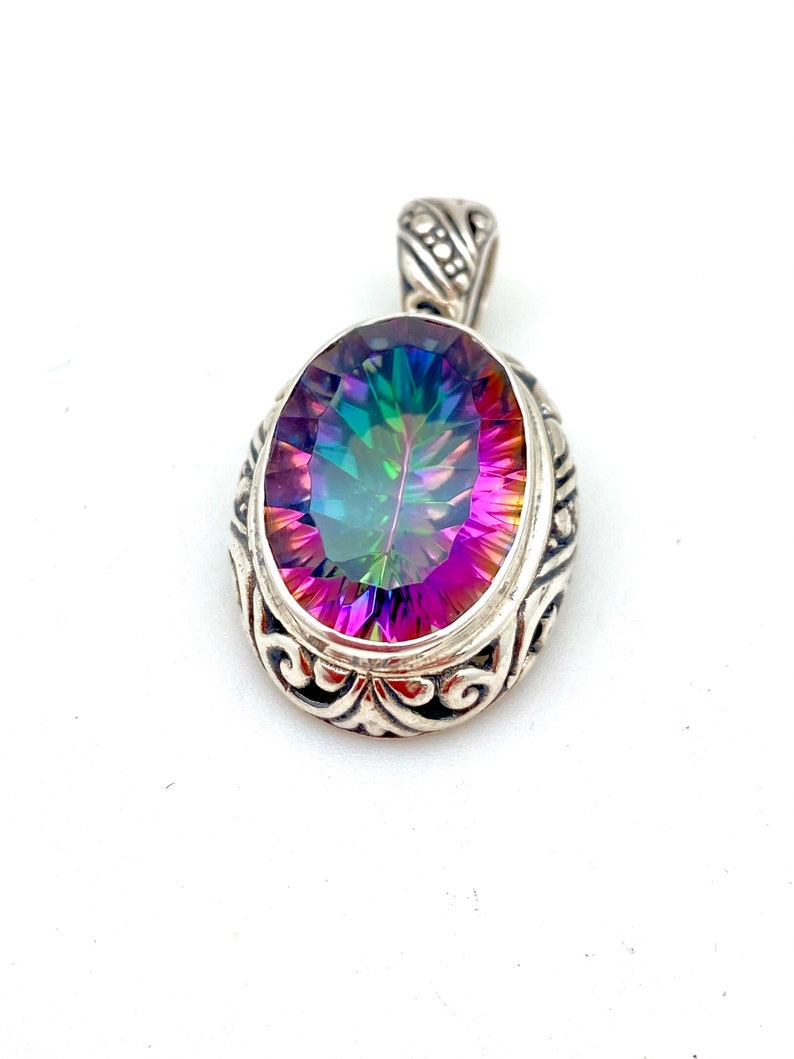 May include: A silver pendant with an oval-shaped iridescent gemstone. The pendant has a detailed filigree design around the gemstone.
