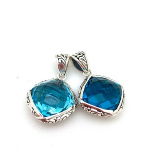 May include: Two silver pendants with blue gemstone accents. The pendants feature an ornate, filigree design around the edges of the gemstones.