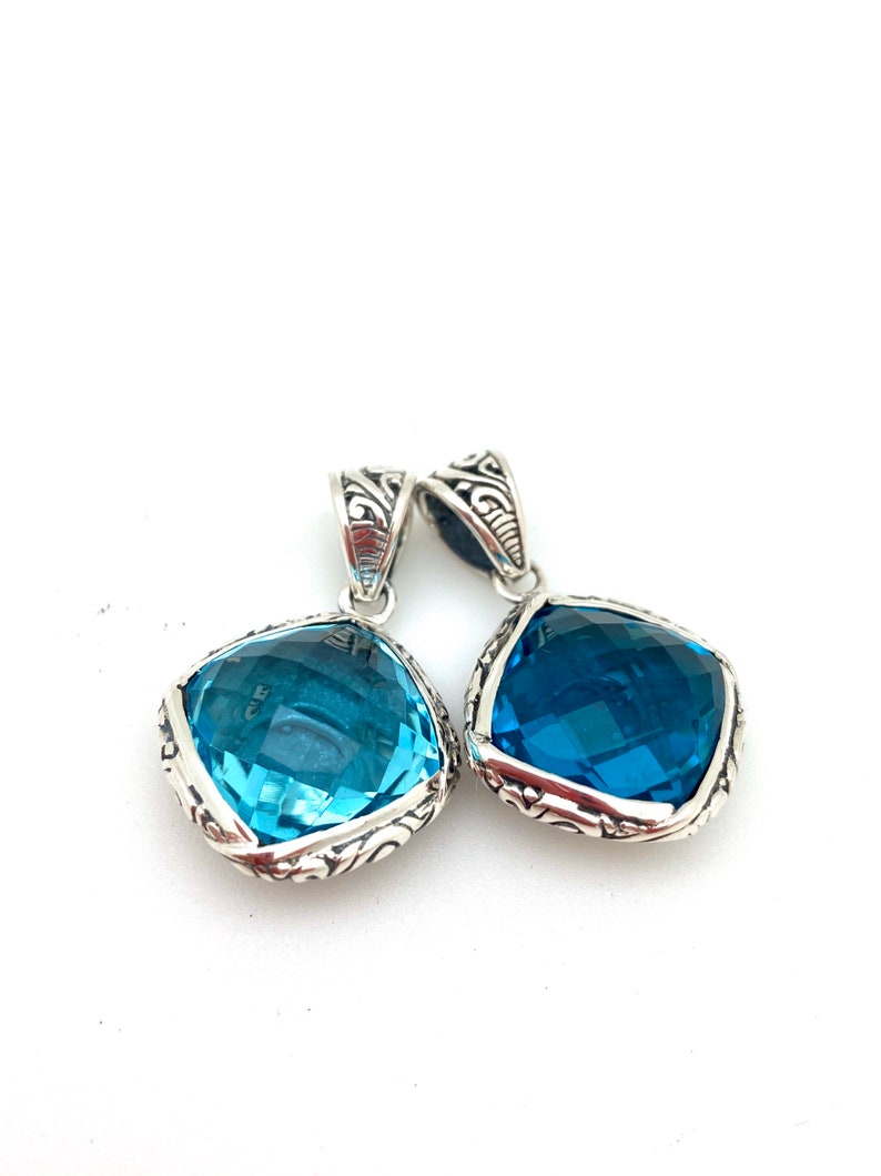 May include: Two silver pendants with blue gemstone accents. The pendants feature an ornate, filigree design around the edges of the gemstones.