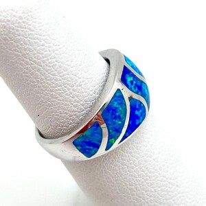 May include: A silver ring with a blue and green opal inlay. The opal is set in a curved band and has a geometric pattern.