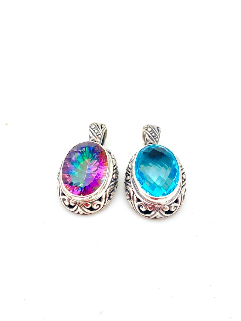 May include: Two silver pendants with oval-shaped gemstones. The pendant on the left has a rainbow-colored gemstone, while the pendant on the right has a light blue gemstone.