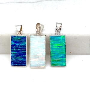 Puede incluir: Tres collares colgantes de plata con piedras de ópalo rectangulares. Los ópalos son azules, blancos y verdes.
